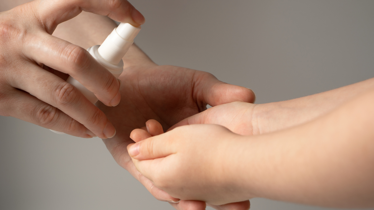 Un adulto disinfetta con il gel igienizzante la manina di un bambino