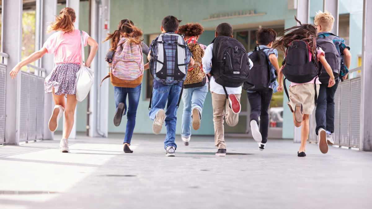 Gruppo di studenti con zaino in spalla corre lungo il corridoio verso l'ingresso della scuola