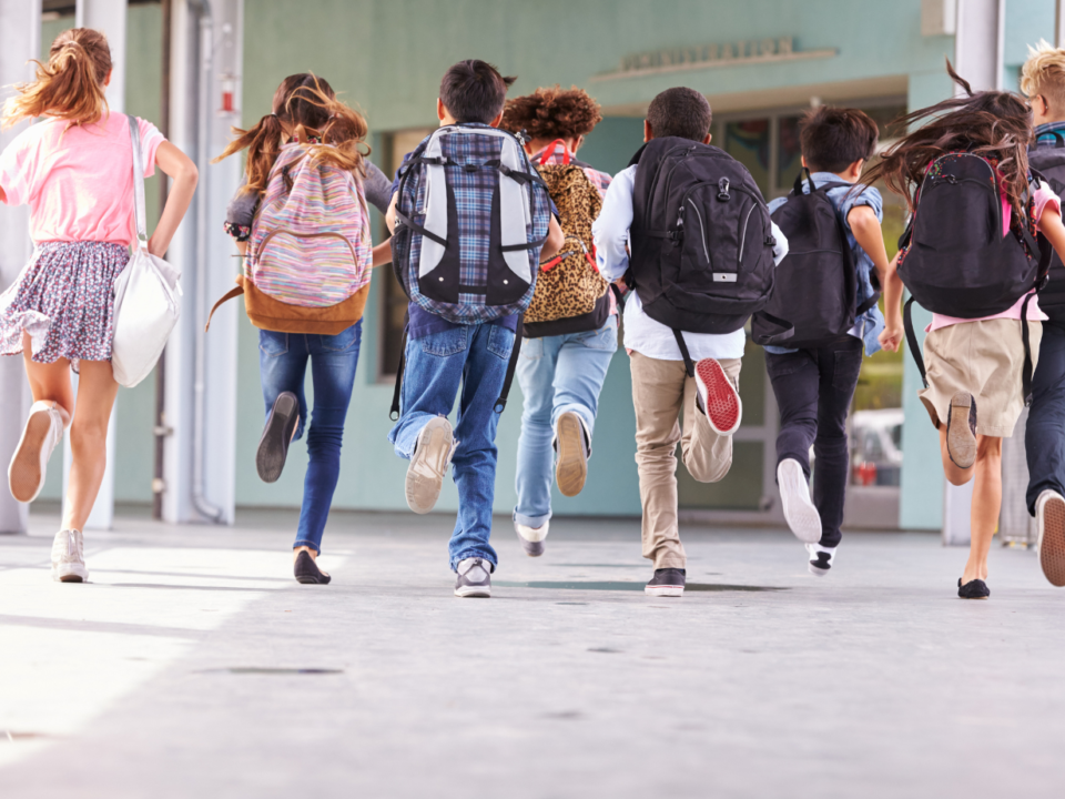 Gruppo di studenti con zaino in spalla corre lungo il corridoio verso l'ingresso della scuola