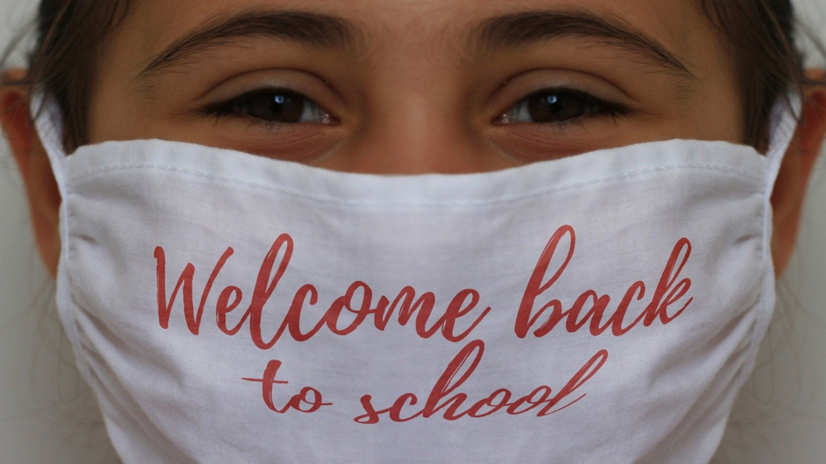 Primo piano di una bambina con mascherina bianca con la scritta «Welcome back to school»