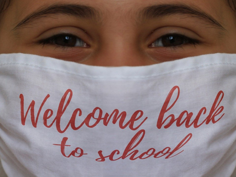 Primo piano di una bambina con mascherina bianca con la scritta «Welcome back to school»