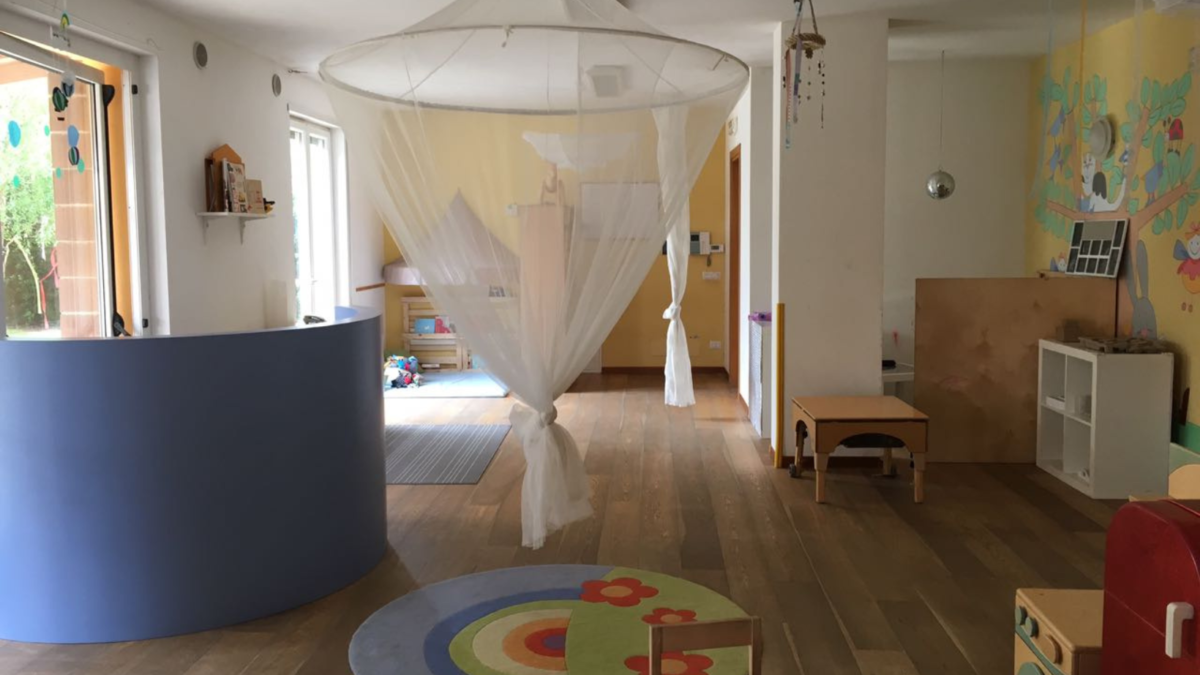 Interno di un nido d'infanzia con zanzariera bianca a baldacchino, tappeto colorato e arredi in legno
