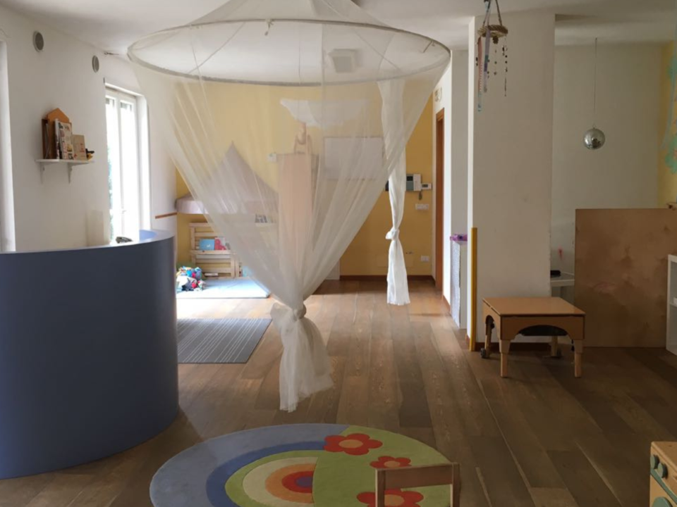 Interno di un nido d'infanzia con zanzariera bianca a baldacchino, tappeto colorato e arredi in legno