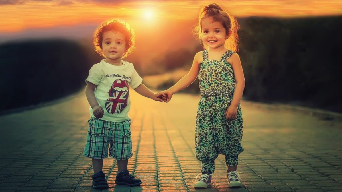 Due bambini piccoli si tengono per mano su un vialetto in pietra al tramonto