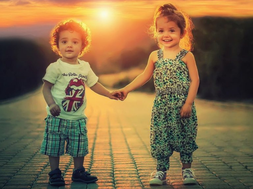 Due bambini piccoli si tengono per mano su un vialetto in pietra al tramonto