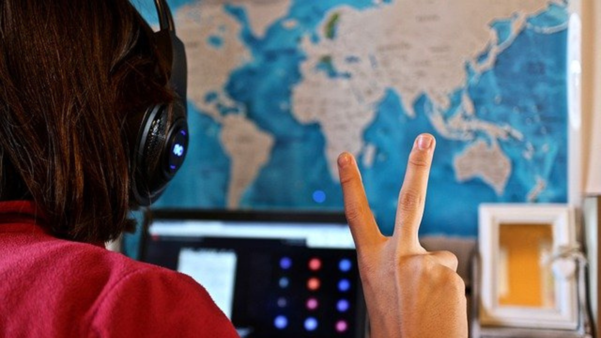 Bambina con cuffie e mappamondo alle spalle fa il segno della vittoria davanti al computer