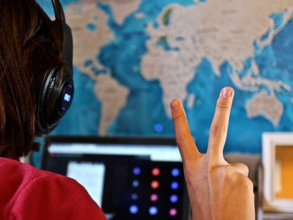 Bambina con cuffie e mappamondo alle spalle fa il segno della vittoria davanti al computer