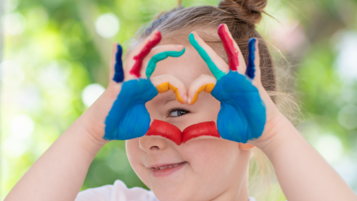 Bambina forma un cuore con le mani dipinte a colori davanti al viso
