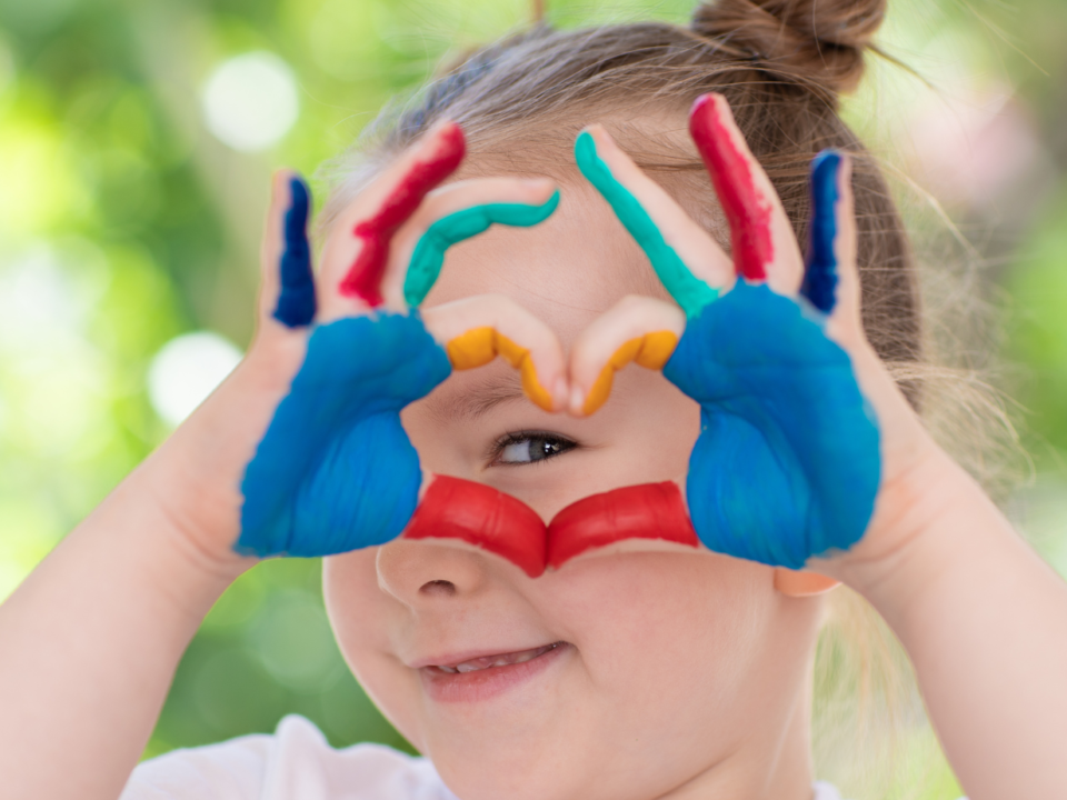 Bambina forma un cuore con le mani dipinte a colori davanti al viso