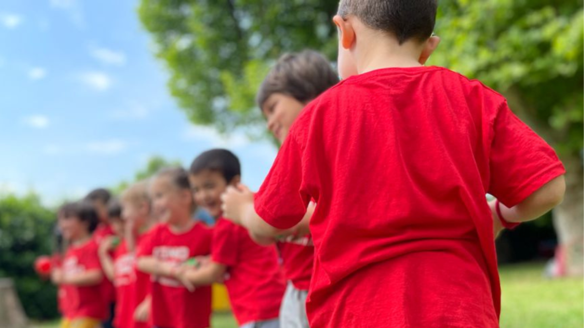 Bambini in maglietta rossa in fila all'aperto durante un'attività sportiva in giardino