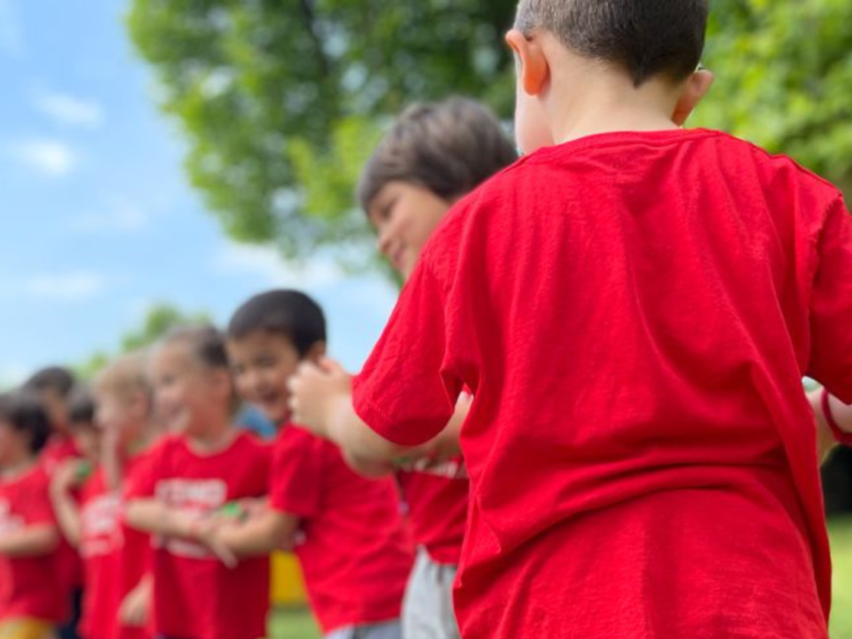 Bambini in maglietta rossa in fila all'aperto durante un'attività sportiva in giardino