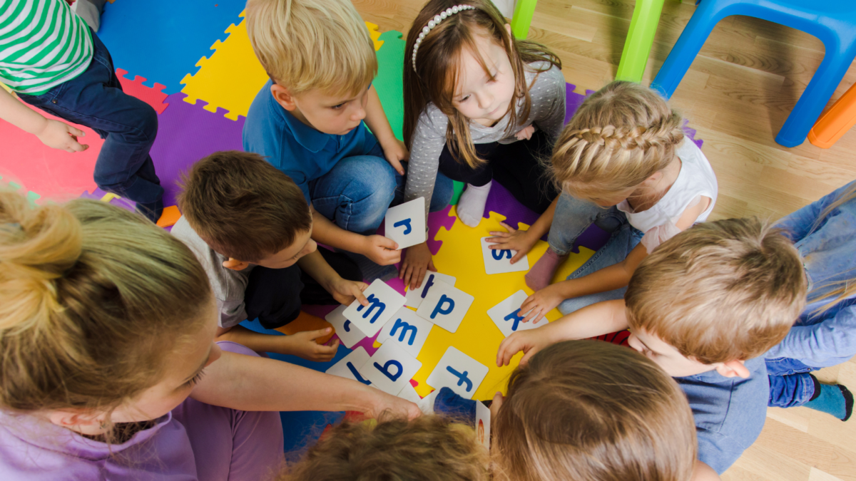 Bambini e un'insegnante giocano con carte alfabetiche colorate sedute in cerchio