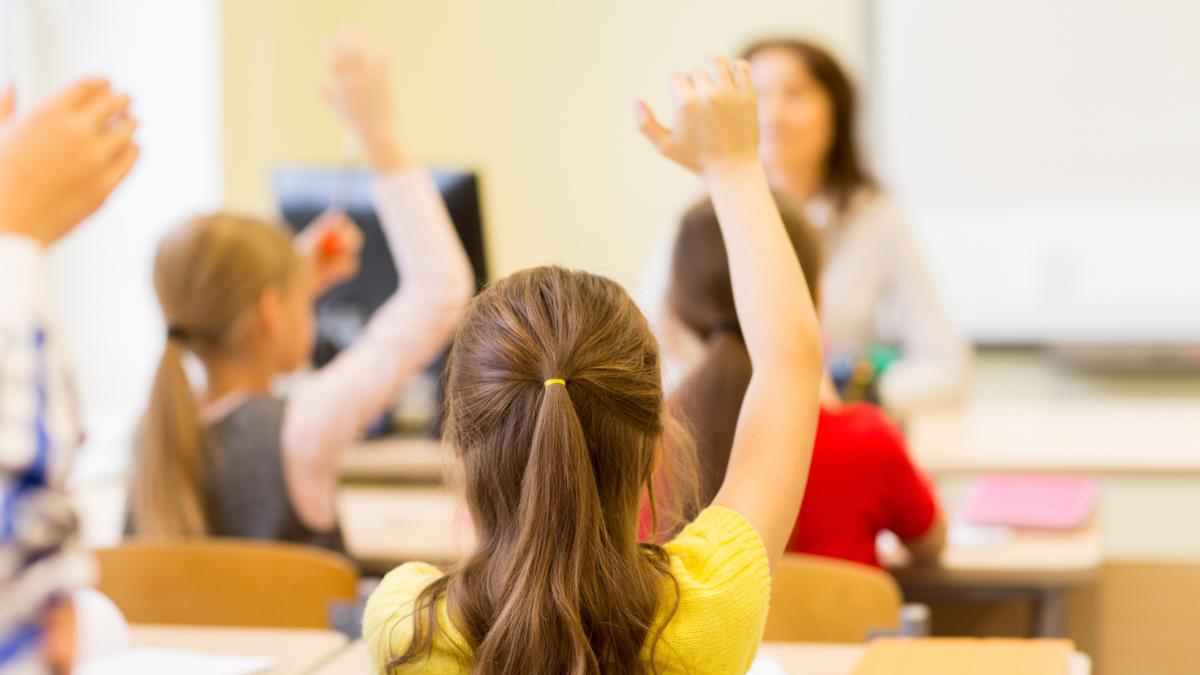 Bambini in classe alzano la mano durante una lezione