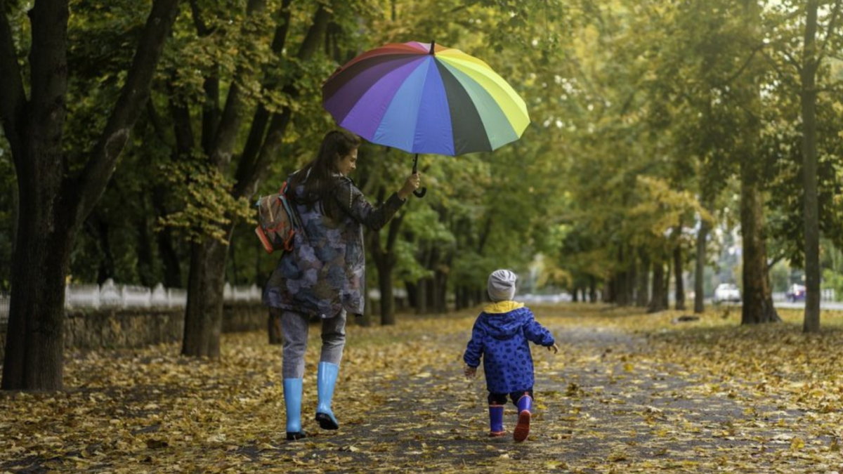 Madre e bambino camminano con un ombrello colorato lungo un viale autunnale