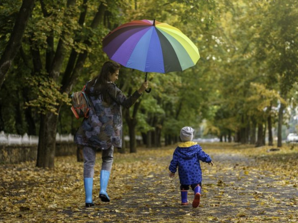 Madre e bambino camminano con un ombrello colorato lungo un viale autunnale