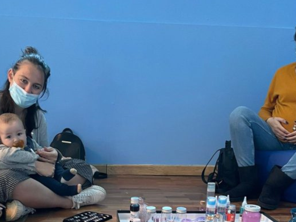Mamme con mascherina sedute a terra durante un incontro del gruppo neomamme, una con un bebè in braccio