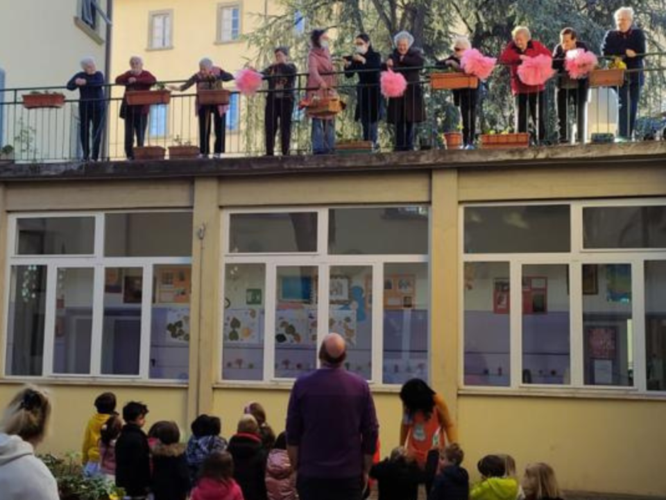 Anziani affacciati al balcone salutano i bambini della scuola riuniti nel cortile