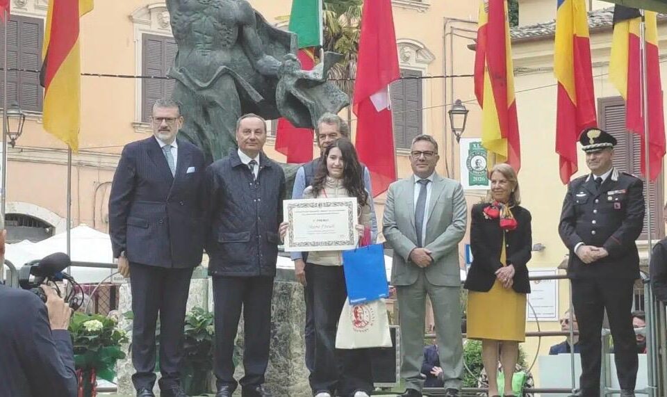 Studentessa premiata con un attestato durante una cerimonia pubblica in piazza, tra autorità e carabinieri
