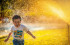 Bambino sorridente corre bagnato tra gli spruzzi d'acqua di un irrigatore in un giorno d'estate
