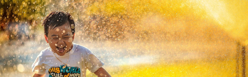 Bambino sorridente corre bagnato tra gli spruzzi d'acqua di un irrigatore in un giorno d'estate