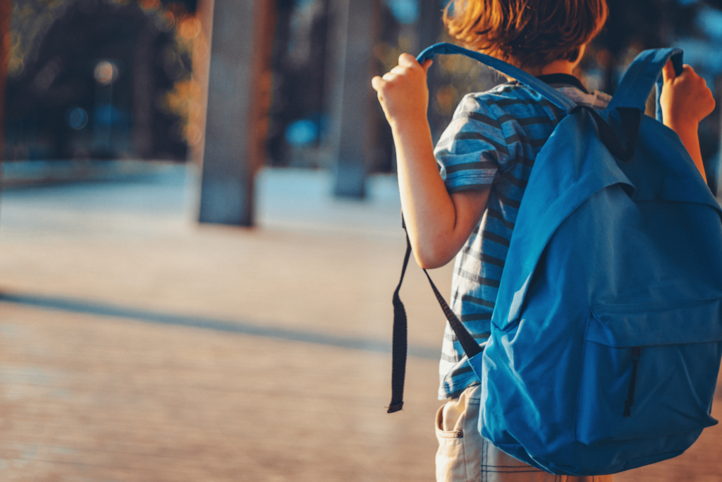 Bambino con zaino blu visto di spalle mentre si avvia verso scuola