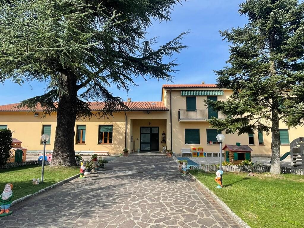 Facciata e giardino della scuola dell'infanzia San Giovanni Bosco di Lama, con alberi e giochi per bambini