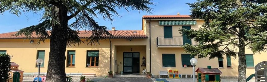 Facciata e giardino della scuola dell'infanzia San Giovanni Bosco di Lama, con alberi e giochi per bambini
