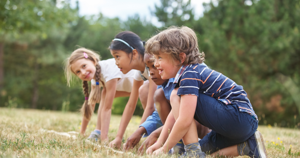 Bambini inginocchiati sull'erba, pronti a partire per una gara all'aperto