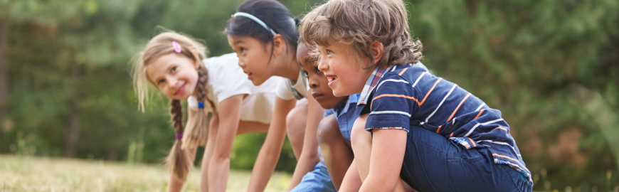 Bambini inginocchiati sull'erba, pronti a partire per una gara all'aperto